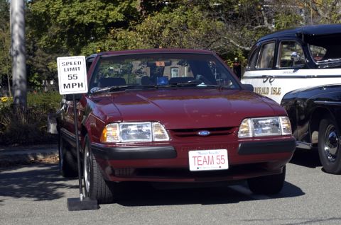 1973 Dodge 1500 - A maroon Ford Mustang is parked next to other vehicles, with a speed limit sign visible.