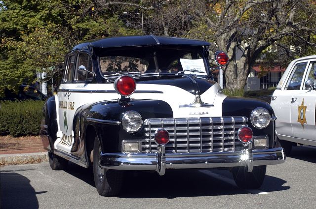 Front view of a black and white police car with "EMERALD ISLE" text on the side. Another police car is partially visible to the right