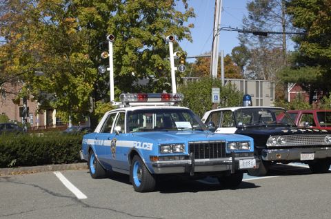 1973 Dodge 1500 - A blue police car is parked next to other vehicles, a prominent light bar and traffic signal apparatus on its roof.