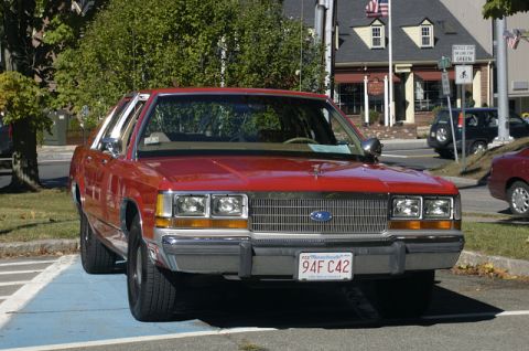 1973 Dodge 1500 - Front view of a red Ford Crown Victoria, parked in a handicapped spot. Another vehicle is visible in the background.