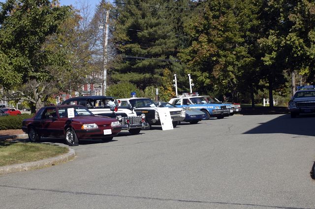 Maroon coupe parked in front of several police cars, angled from the front
