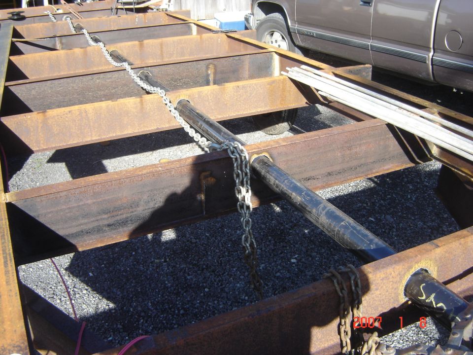 Trailer frame with chains and a brown pickup truck in the background