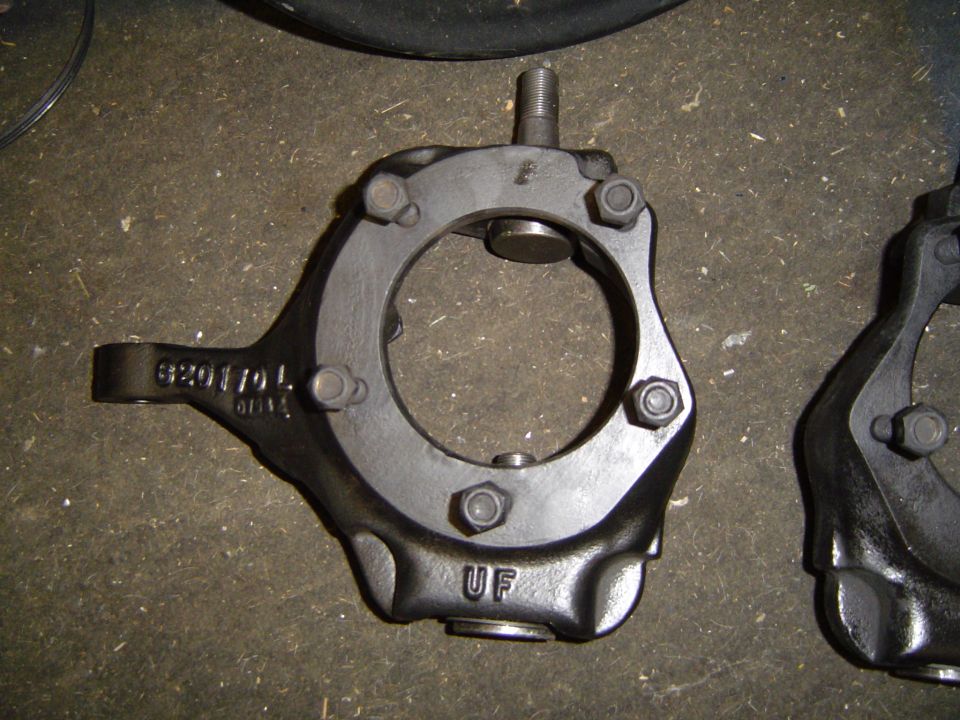 Black-painted cast steering knuckle marked 620117 L and UF on a garage floor