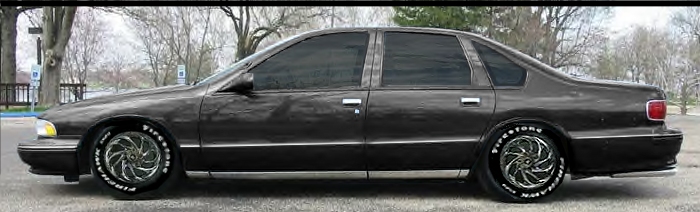 Charcoal full-size sedan, side view, lowered on chrome swirl wheels with white-letter tires