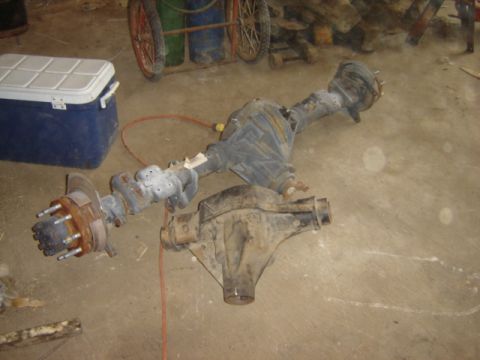 1992 Ford Bronco - Two vehicle axles are laid out on a concrete floor, with a blue cooler and cart in the background.