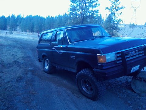1988 Ford Bronco - Dark blue full-size Ford Bronco with its removable hardtop in place, photographed from the driver-side 3/4 front on a frosty dirt two-track…