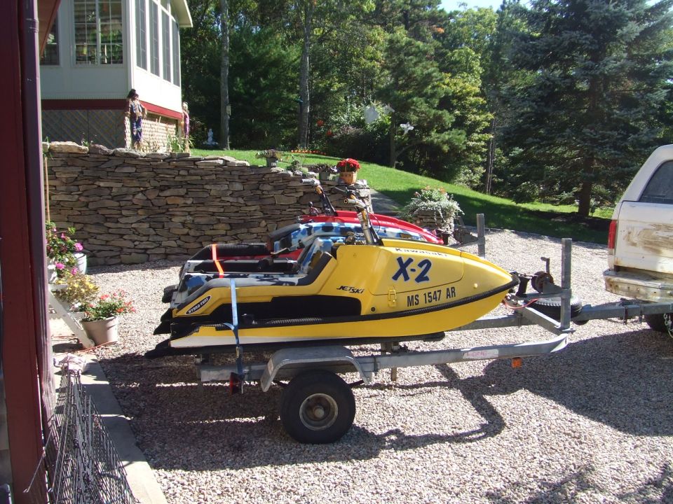 Yellow Kawasaki X-2 stand-up Jet Ski strapped on a trailer in a gravel driveway