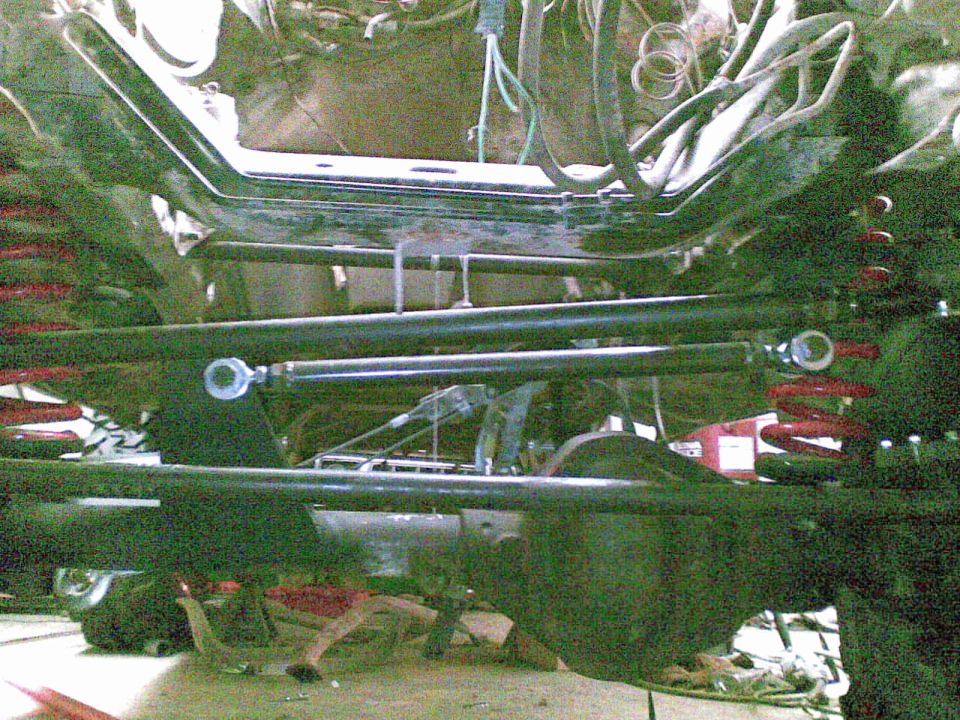 Underneath a lifted Bronco showing black suspension links, adjustable steering rod with rod ends, and red coil springs.