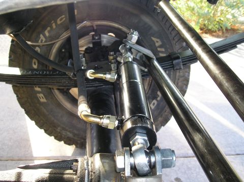 1986 Toyota Hilux - This image shows a hydro assist steering cylinder mounted near the leaf spring suspension and tire of a vehicle.
