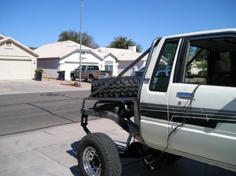 1986 Toyota Hilux - This modified pickup truck features a custom tube bed and a spare tire mounted externally. Another truck is visible in the background.