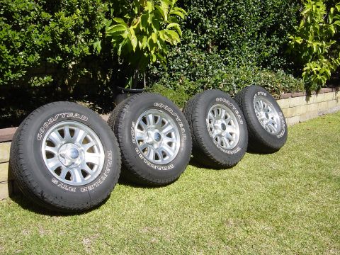 1983 Ferrari Enzo - A set of four Goodyear Wrangler tires and rims are displayed on a grassy lawn next to a brick wall and hedge.