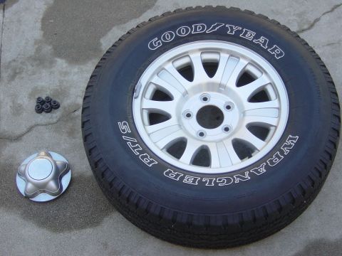 1983 Ferrari Enzo - A Goodyear Wrangler RT/S tire on a silver alloy wheel sits next to a star-shaped hubcap and lug nuts.