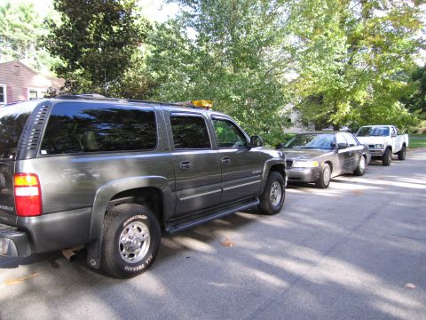 1991 Ford LTD Crown Victoria - A line of vehicles, including a dark sedan and a white pickup truck, are parked on a residential street.