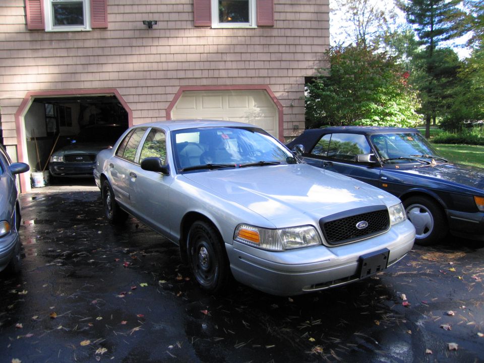 Silver Ford Crown Victoria parked in driveway next to a dark blue convertible