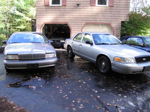 1991 Ford LTD Crown Victoria - Two sedans and a convertible are parked in a driveway in front of a house with an open garage.