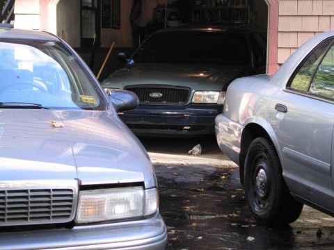 1991 Ford LTD Crown Victoria - A dark blue Ford Crown Victoria is parked in a garage, partially obscured by other vehicles.