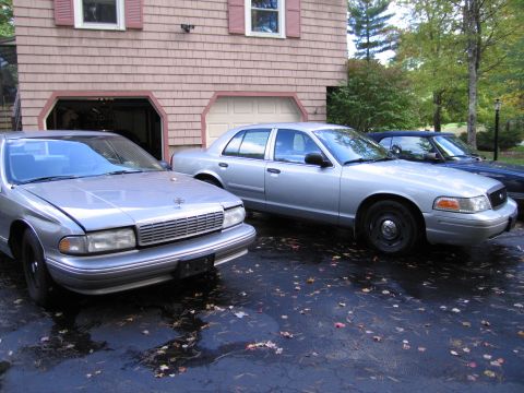 1991 Ford LTD Crown Victoria - A silver sedan is parked in a driveway next to another vehicle, with a house in the background.