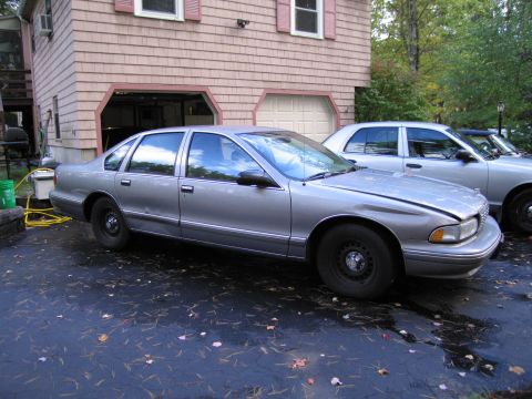 1991 Ford LTD Crown Victoria - Two silver sedans are parked in a driveway in front of a house with an open garage.