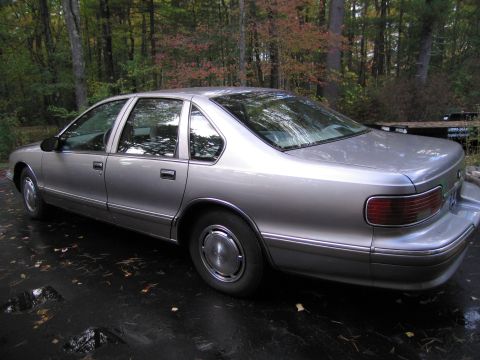1991 Ford LTD Crown Victoria - A silver 1991 Chevrolet Caprice sedan is parked outdoors on a wet, leaf-strewn surface.