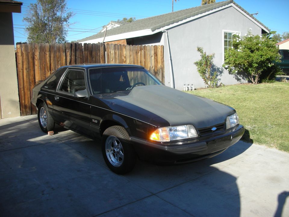 Front three-quarter of a black Fox-body Mustang with primer hood