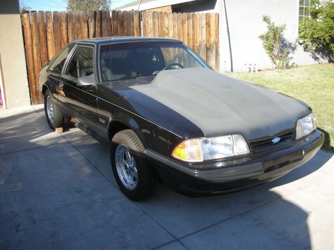 1998 Ford Crown Victoria - This black Ford Mustang features a prominent grey hood scoop and is captured from a 3q-front angle.