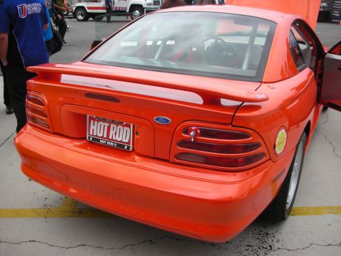 1998 Ford Crown Victoria - Rear view of an orange Ford Mustang, likely a 1996 model, with a custom license plate.