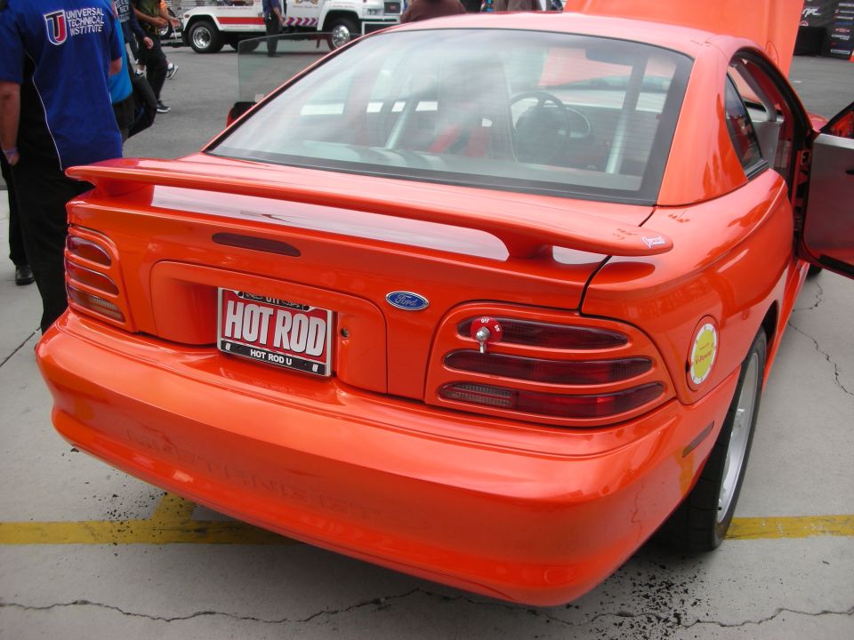 Rear of orange Ford Mustang coupe with HOT ROD plate at car show