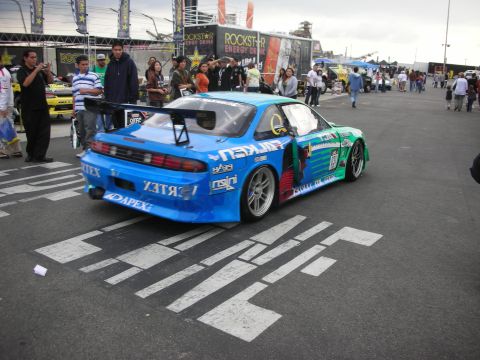 1998 Ford Crown Victoria - A modified Nissan Silvia S14 drift car is parked on the asphalt with white line markings.