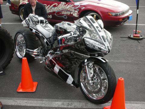 1998 Ford Crown Victoria - A highly customized motorcycle is parked next to a red car with graphics.