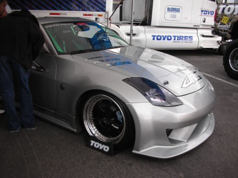 1998 Ford Crown Victoria - A modified Nissan 350Z is displayed at an event, with a large truck in the background.