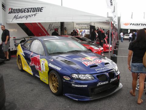 1998 Ford Crown Victoria - A blue Pontiac GTO race car, sponsored by Red Bull and Bridgestone, is parked under a tent with other vehicles.