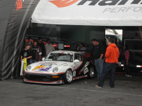 1998 Ford Crown Victoria - A white Porsche 911 race car is parked under a tent with several people standing nearby.