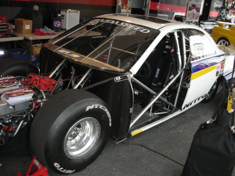 1998 Ford Crown Victoria - Drag racing car interior shows roll cage, racing seat, and large slick tire. "MAZDASPEED" is on the windshield.