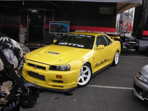 1998 Ford Crown Victoria - A yellow Nissan Skyline GT-R R34 is parked in a garage area next to another car.