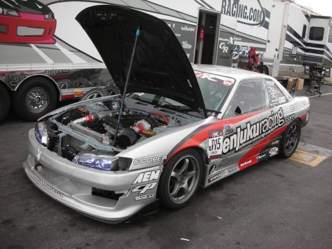 1998 Ford Crown Victoria - A silver racing coupe with its hood open, revealing the engine and adorned with various sponsor decals.