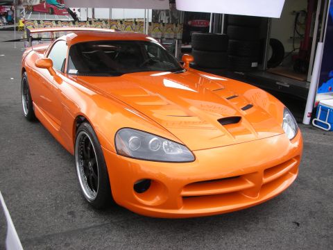 1998 Ford Crown Victoria - This orange sports car is parked on asphalt, with a trailer and tires visible in the background.