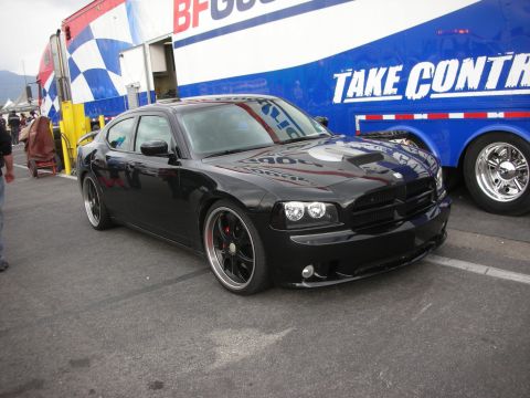 1998 Ford Crown Victoria - Black Dodge Charger with custom wheels parked beside a trailer at an event.