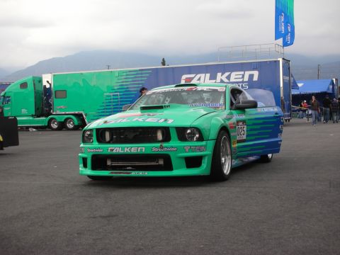 1998 Ford Crown Victoria - A race-prepped Ford Mustang with prominent sponsor decals sits in a parking lot next to a large semi-truck.