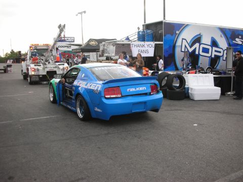 1998 Ford Crown Victoria - A blue Ford Mustang with racing decals is being towed by a tow truck at an event.