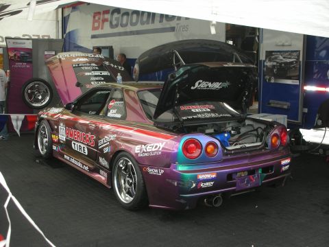 1998 Ford Crown Victoria - A highly customized Nissan Skyline GT-R R34 is displayed with its hood and trunk open, racing sponsorships.