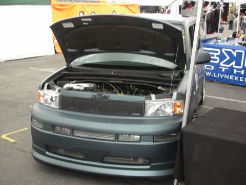 1998 Ford Crown Victoria - Teal Scion xB with hood open, showing aftermarket modifications to the engine bay and front end.