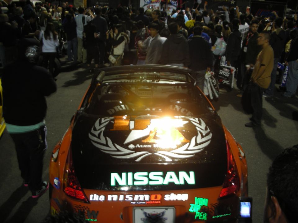 Rear of orange Nissan 350Z with NISMO decals in night crowd