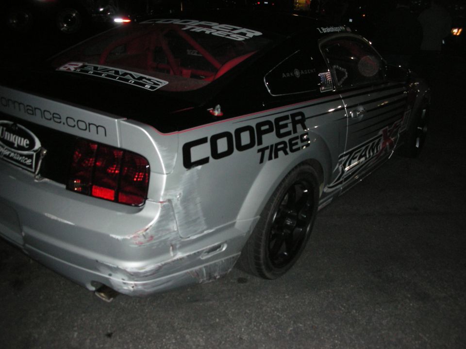 Rear of damaged silver Cooper Tires Mustang race car at night
