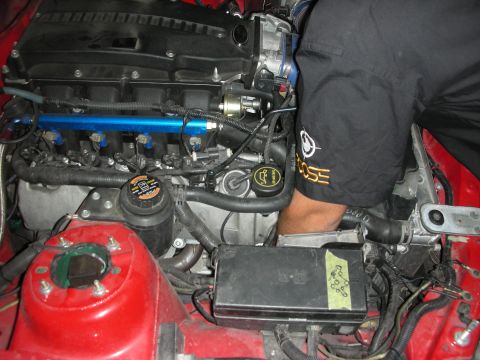 1998 Ford Crown Victoria - A mechanic is working on the engine of a car, with a blue fuel rail prominently displayed.