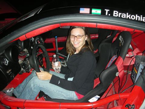 1998 Ford Crown Victoria - A woman smiles while sitting in the driver's seat of a race car, which features a roll cage and racing seats.