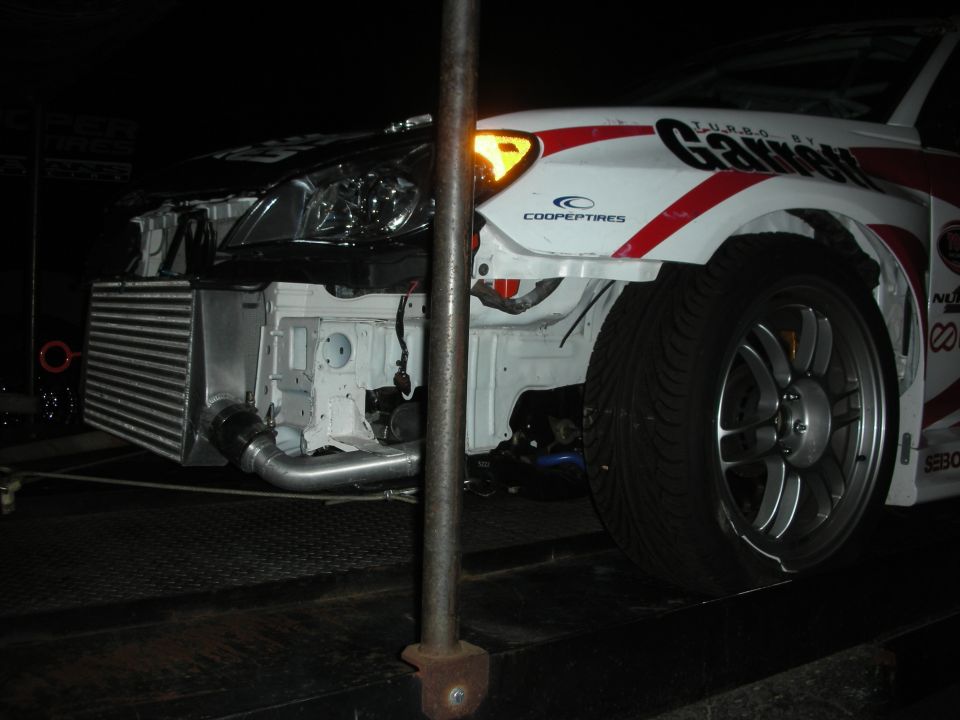 Front end of a white race car on a trailer at night with bumper removed exposing intercooler