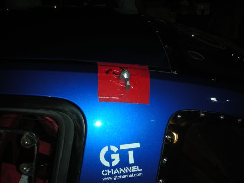 1998 Ford Crown Victoria - Close-up of a blue car's fender showing a GT CHANNEL logo and red tape with a bolt.