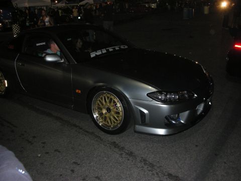 1998 Ford Crown Victoria - A gray coupe with distinctive gold rims and a Nitto banner is seen at an event.
