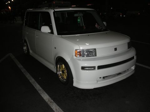 1998 Ford Crown Victoria - A white box car with custom gold rims is seen parked in a lot at night.
