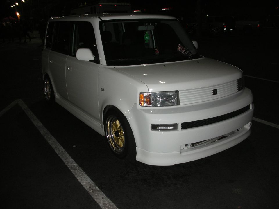 Front three-quarter of a white boxy compact car at night with gold wheels